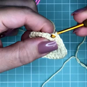 Mão de uma artesã tecendo com agulha de crochê e linha colorida